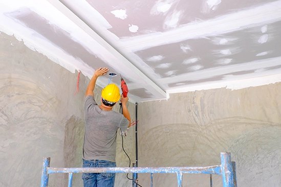Workers lifting drywall panels onto studs inside unfinished residential interior