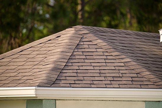 Close-up of roofer nailing new shingles along roof ridge in daylight